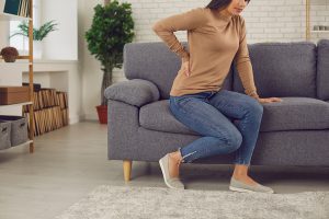Young woman wants to get up from the sofa but feels a sudden pain in her lower back