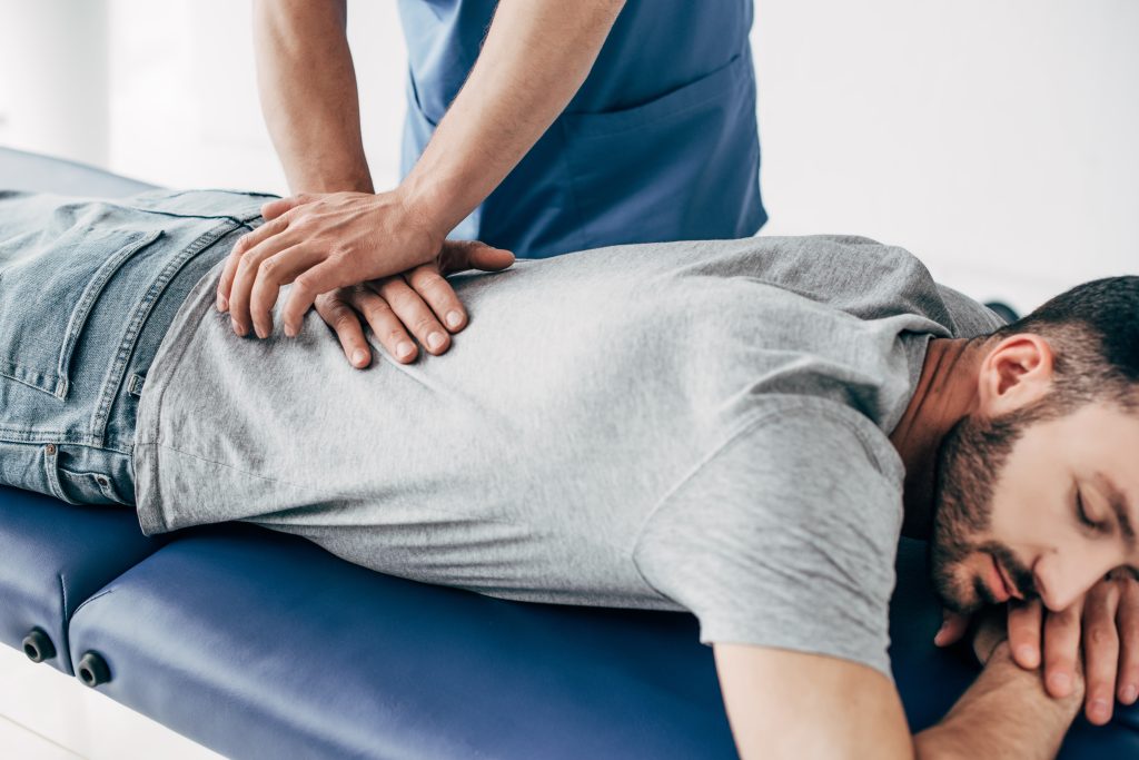 chiropractor massaging back of man on Massage Table in clinic